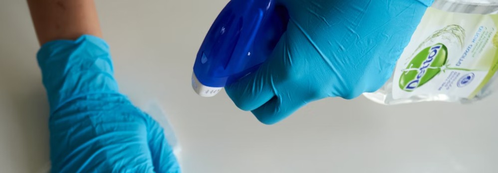 Hand med blå rengöringshandske sprayar rengöringsmedel på en yta.